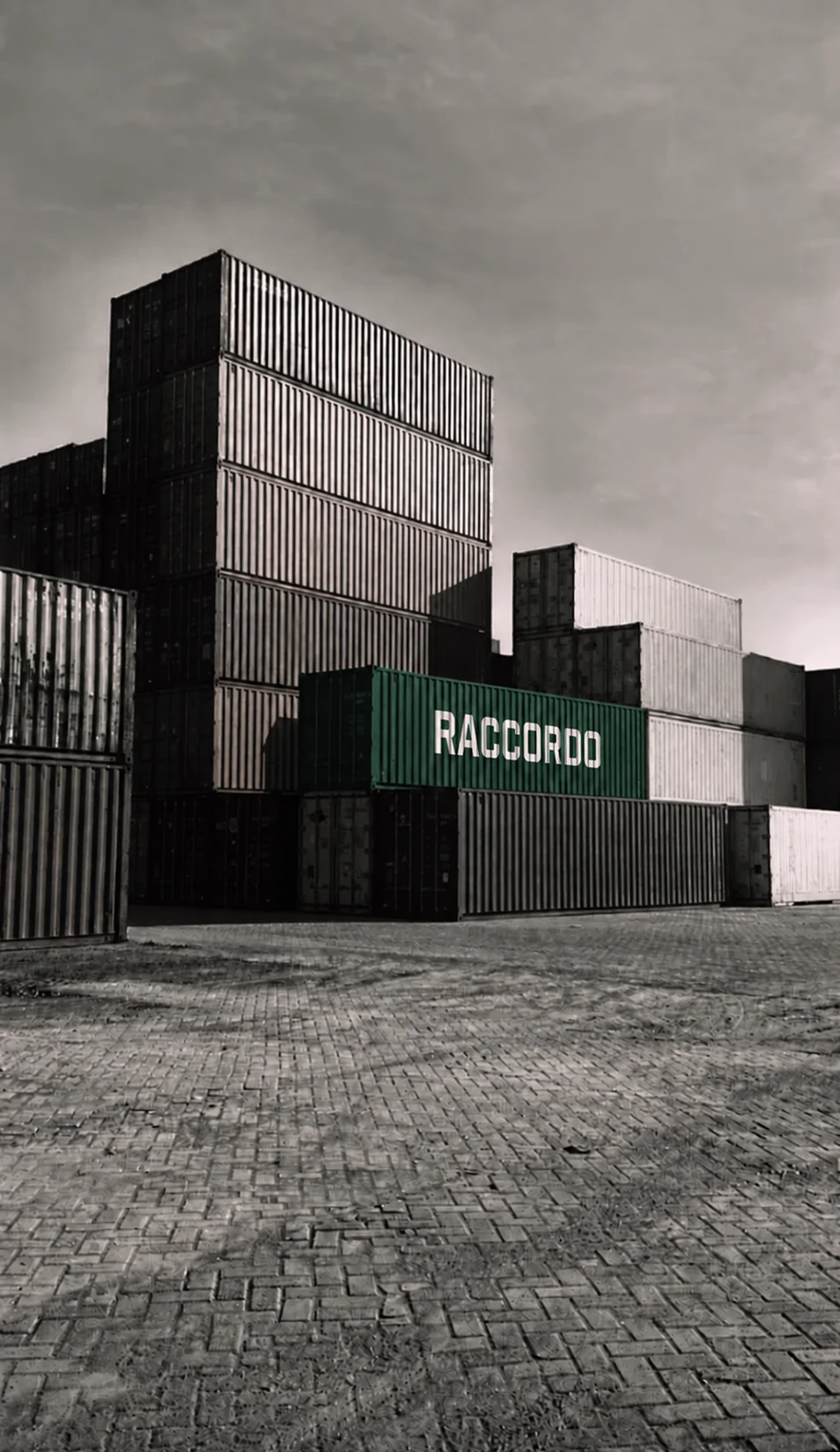 A deep green Raccordo-branded container among monochrome stacked shipping containers